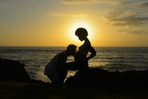 Silhouette of a couple embracing pregnancy at sunset by the ocean, expressing love and expectation.