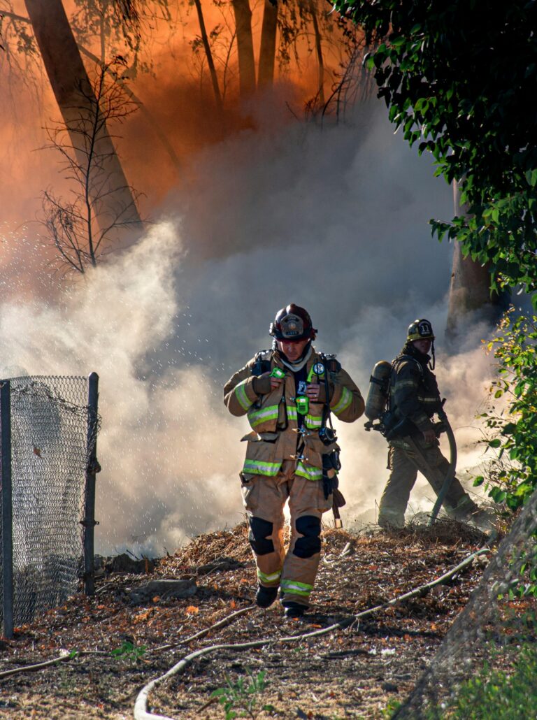 Firefighters in protective gear extinguishing a forest fire with thick smoke and flames.