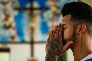 A man with tattoos prays inside a church, capturing a moment of reflection and spirituality.