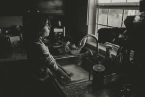 A child washes hands at the kitchen sink in moody black and white lighting.