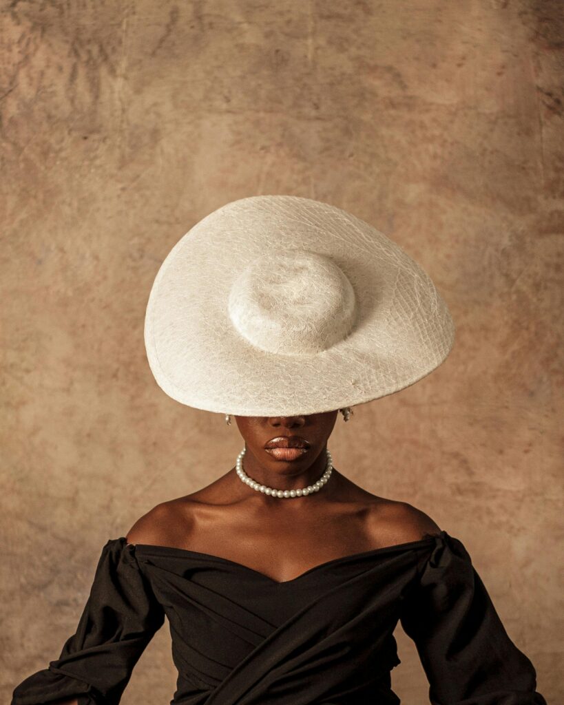 Stylish portrait of an elegant woman wearing a large white hat and pearls.