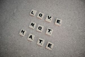 Scrabble tiles on pavement spelling 'LOVE NOT HATE', promoting positivity.