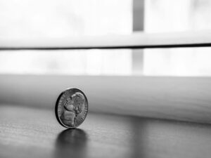 Monochrome close-up of a standing coin reflecting on a smooth surface.