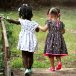 Two young girls in colorful dresses walking hand in hand outdoors, embodying friendship and innocence.