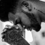 A man in deep thought and prayer, showcasing tattoos and an earring in a powerful black and white image.