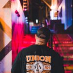 Man in ironworker union shirt walking up colorful urban stairs at night.