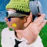 A man outdoors wearing headphones and fun accessories, gesturing with interest. Perfect for music or lifestyle themes.