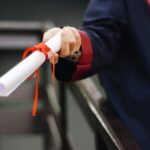A close-up image of a graduate holding a diploma tied with a red ribbon, symbolizing achievement and success.