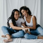 Two smiling women sitting and laughing together in casual jeans and tops, capturing friendship and joy.