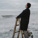 Woman standing on a ladder gazing at the ocean on an overcast day.