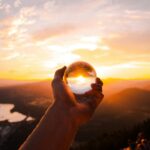 Captivating sunset view reflected in a crystal ball held by hand, overlooking a scenic landscape.