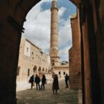 A view of the historic Mardin Ulucamii Mosque and its famous minaret in Türkiye, framed by architectural arches.