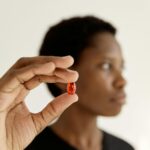 Portrait of a thoughtful woman holding a red pill in focus. Studio shoot against a white background.