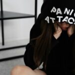 A woman sitting with 'PANIC ATTACK' on her hood, showing anxiety indoors.