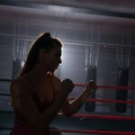 Silhouette of a female boxer practicing inside a dimly lit gym, showcasing strength and determination.