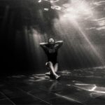 Black and white underwater shot of a woman in a peaceful pose, capturing light play.