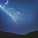 Majestic lightning bolts illuminate the night sky over a silhouetted mountain range.