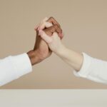 Close-up of two diverse hands gripping in a gesture of unity on a neutral background.