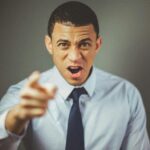 Close-up of an angry businessman in a tie expressing frustration and pointing.