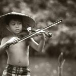 A young boy with a traditional hat plays the violin outdoors, showcasing musical talent and passion.