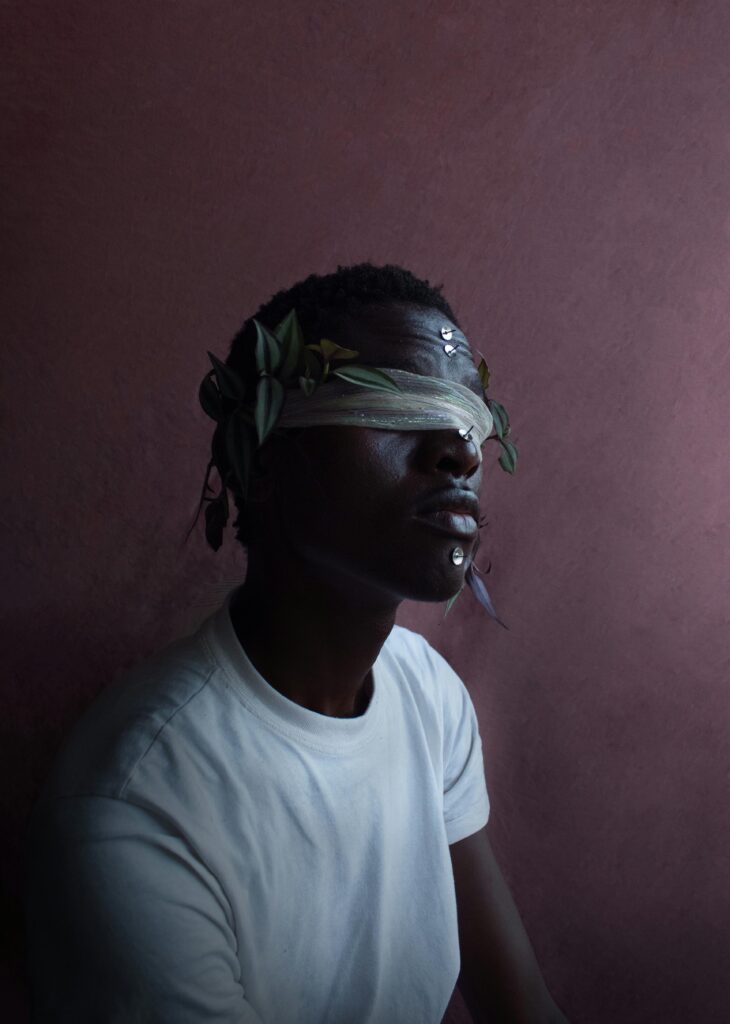 Conceptual portrait of a blindfolded man with leaf adornments, creating a moody and artistic atmosphere.