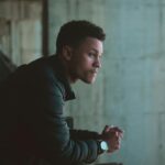 Young adult man leaning on metal railing looking pensive, wearing casual attire.