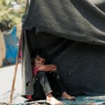 A young boy sitting in a makeshift shelter in Gaza, displaying resilience and solitude.