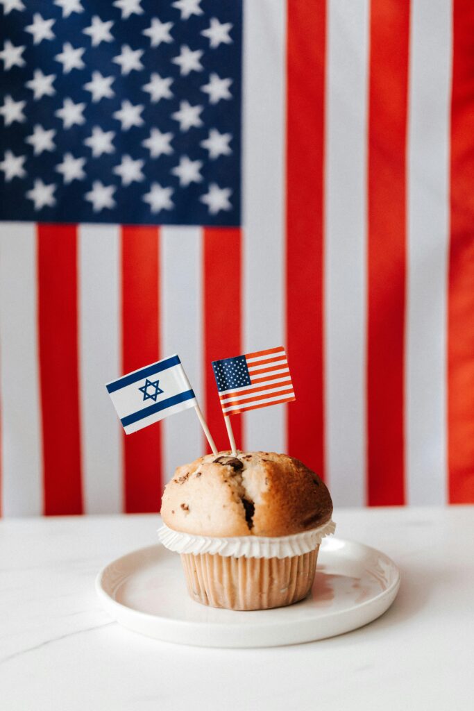 A muffin with American and Israeli flags against USA flag backdrop, symbolizing international relations.