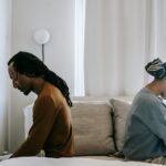 Side view unhappy sorrowful African American couple sitting on bed back to back after having argument
