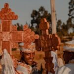Men in traditional Ethiopian clothing holding ornate wooden crosses during a vibrant outdoor ceremony.