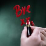Handwriting 'bye' on a mirror with red lipstick, evoking themes of farewell and emotion.